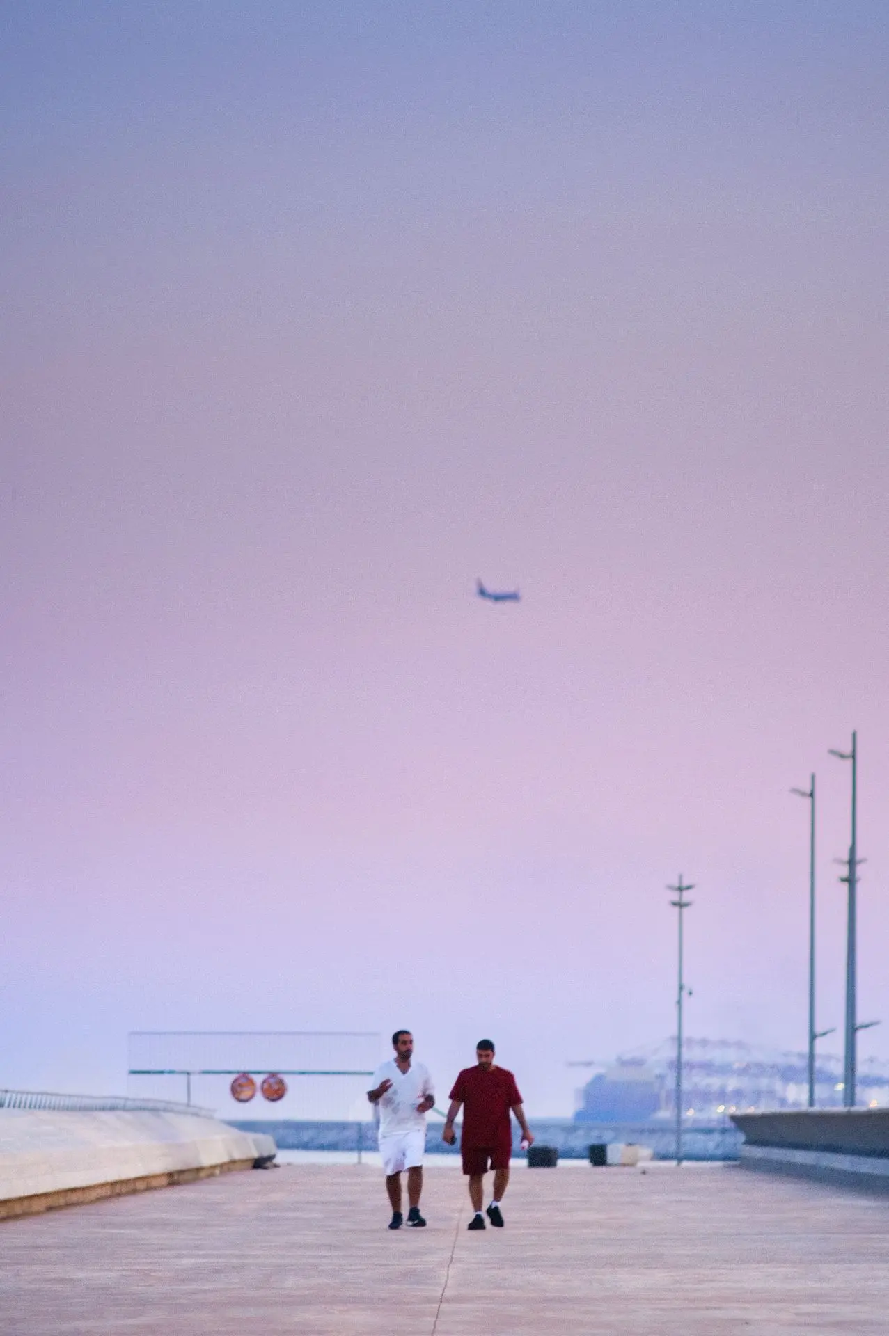 Dos hombres caminan en un entorno minimalista, donde el cielo en tonos pastel se funde con el horizonte marítimo. Una escena que captura la tranquilidad y la energía de una tarde en Barcelona, equilibrando la arquitectura moderna con la conexión humana.