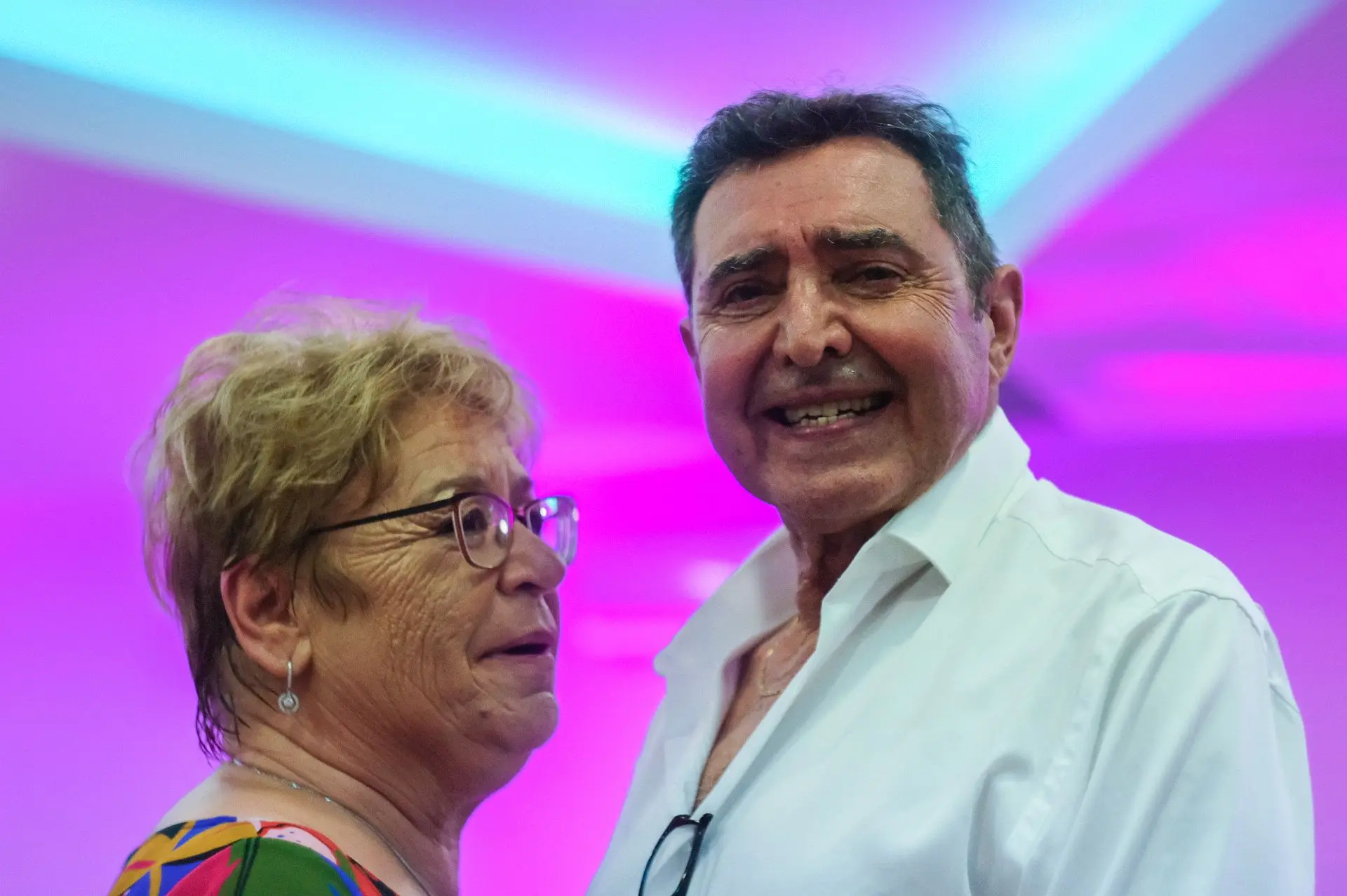 Este retrato captura un instante espontáneo y lleno de significado entre una pareja recién casada. La mirada directa del esposo hacia el objetivo, acompañada de una sonrisa sutil pero sincera, transmite calidez, confianza y una alegría serena. Su expresión contrasta con la presencia parcial de su pareja, agregando profundidad e intriga a la composición. La maestría del fotógrafo se evidencia en el uso de la luz natural, que suaviza la escena y realza la emoción sin distracciones. El encuadre logra una sensación de intimidad y atemporalidad, invitando al espectador a sumergirse en la conexión de la pareja. Más que una simple imagen, esta fotografía encapsula un sentimiento, una complicidad y un instante fugaz de pura felicidad.
