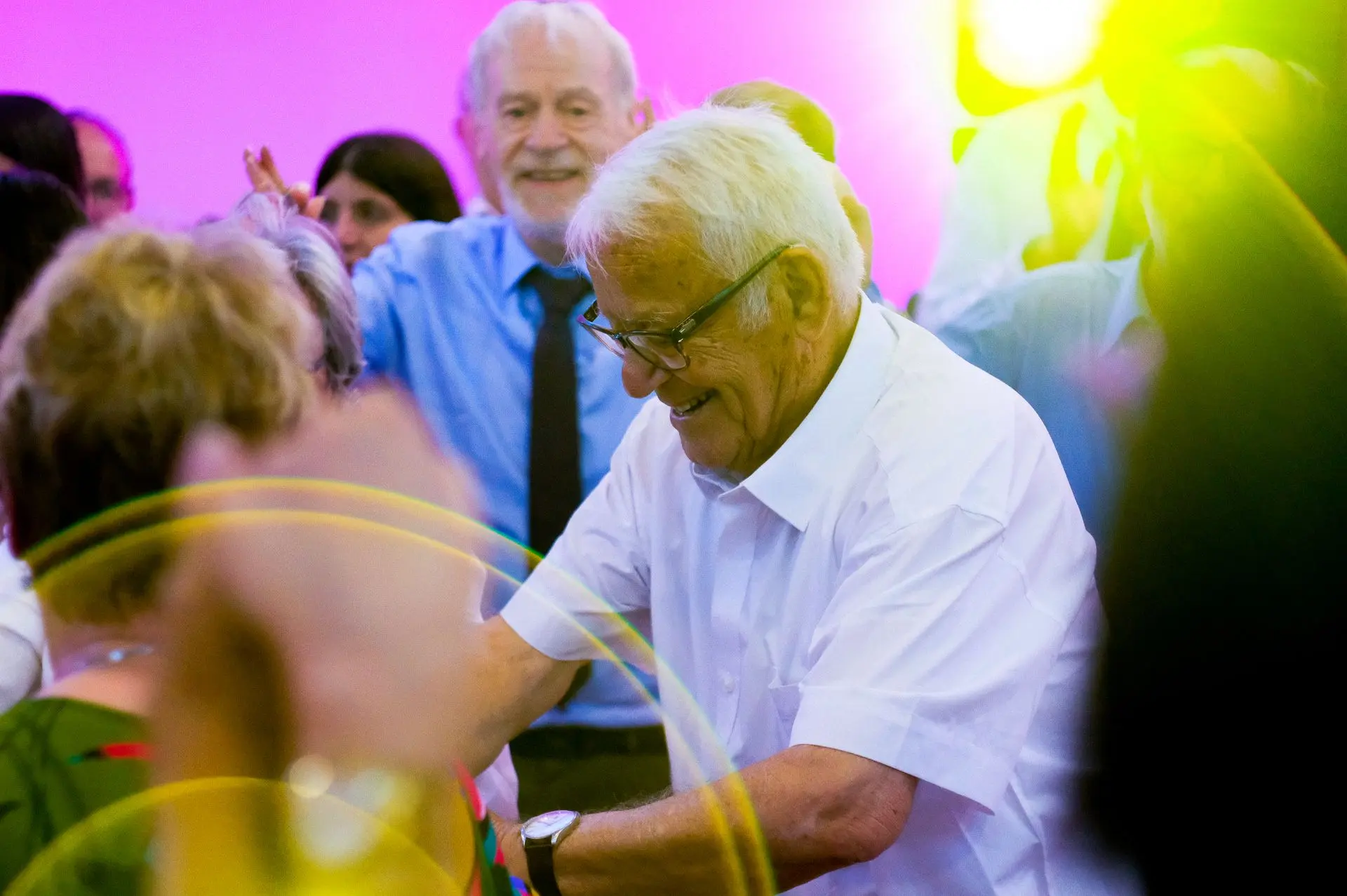 Esta imagen captura la belleza del movimiento más allá de la edad, donde la experiencia y la alegría convergen en un baile que trasciende el tiempo. La bailarina mayor se convierte en el símbolo de la celebración, recordándonos que las bodas no solo marcan nuevos comienzos, sino que también honran el camino recorrido. La fotografía transmite una sensación de nostalgia y resiliencia, con el juego de luces y sombras que añade profundidad a las emociones presentes. En el contexto de Barcelona, esto también refleja las arraigadas tradiciones festivas de la ciudad, donde el baile es un lenguaje universal de conexión y vitalidad.